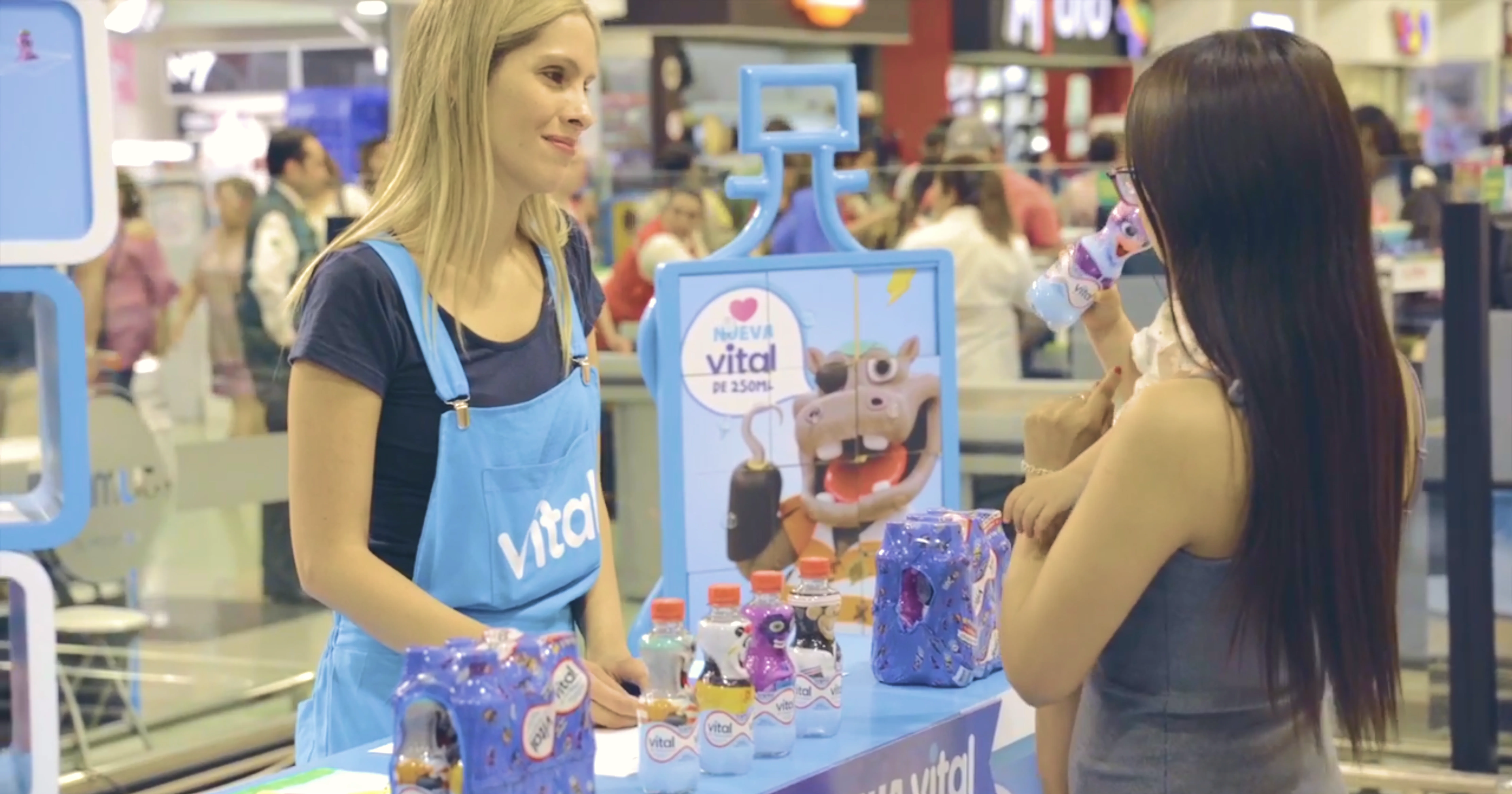 Promotora Vital Kids mostrando una botella Vital con el personaje ave a una clienta en el punto de venta.